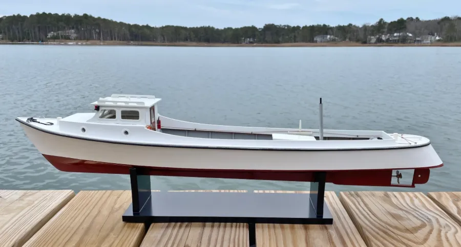 Blackway Draketail Workboat model, white with red bottom paint, on its black stand on a wooden dock over the Bay